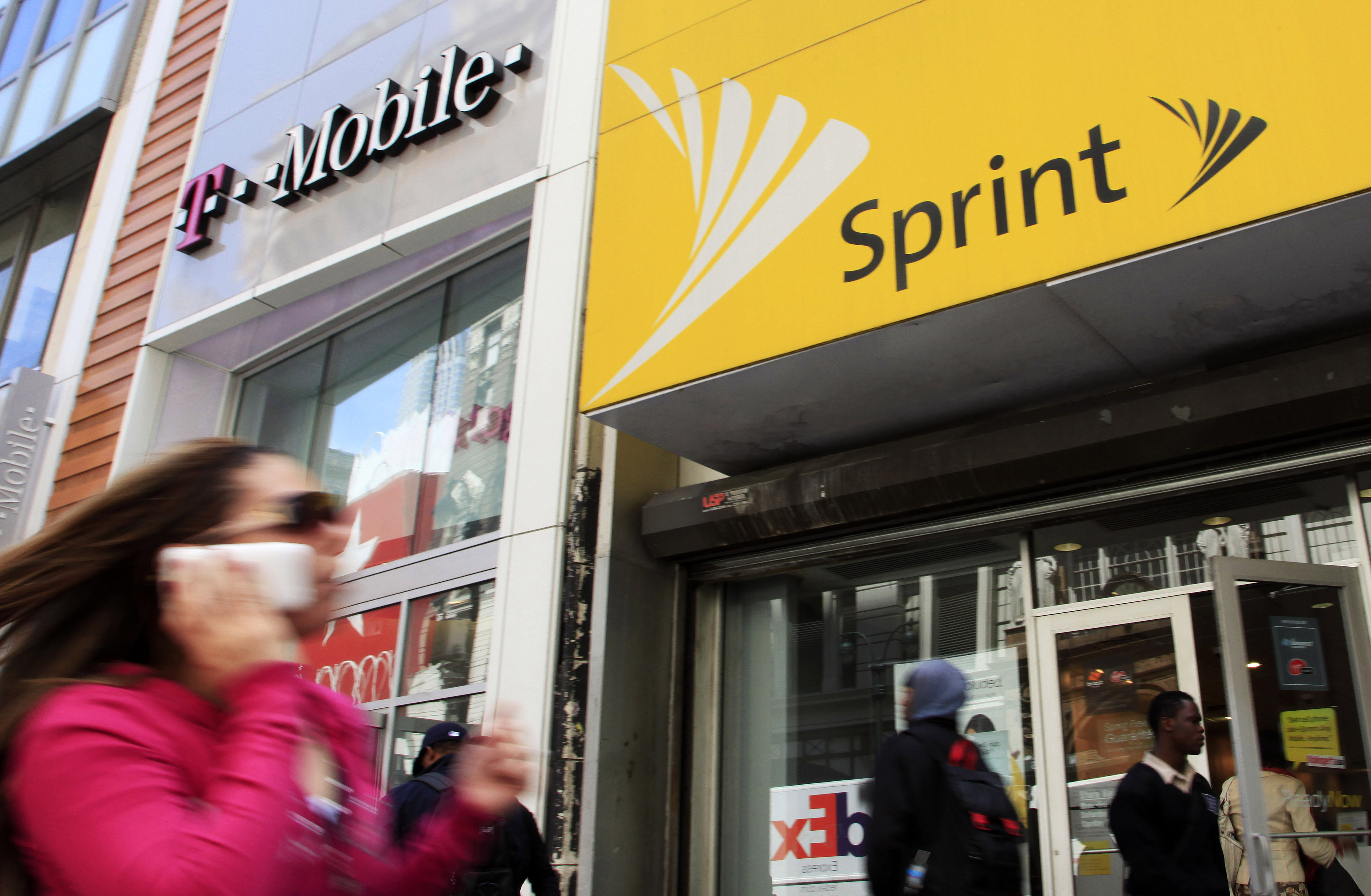 A woman using a cell phone walks past T-Mobile and Sprint stores, Tuesday, April 27, 2010, in New York. Sprint Nextel Corp. on Wednesday, April 28, said it lost a net 75,000 subscribers in the first three months of 2010, compared to a loss of 182,000 in the same quarter last year.(AP Photo/Mark Lennihan)