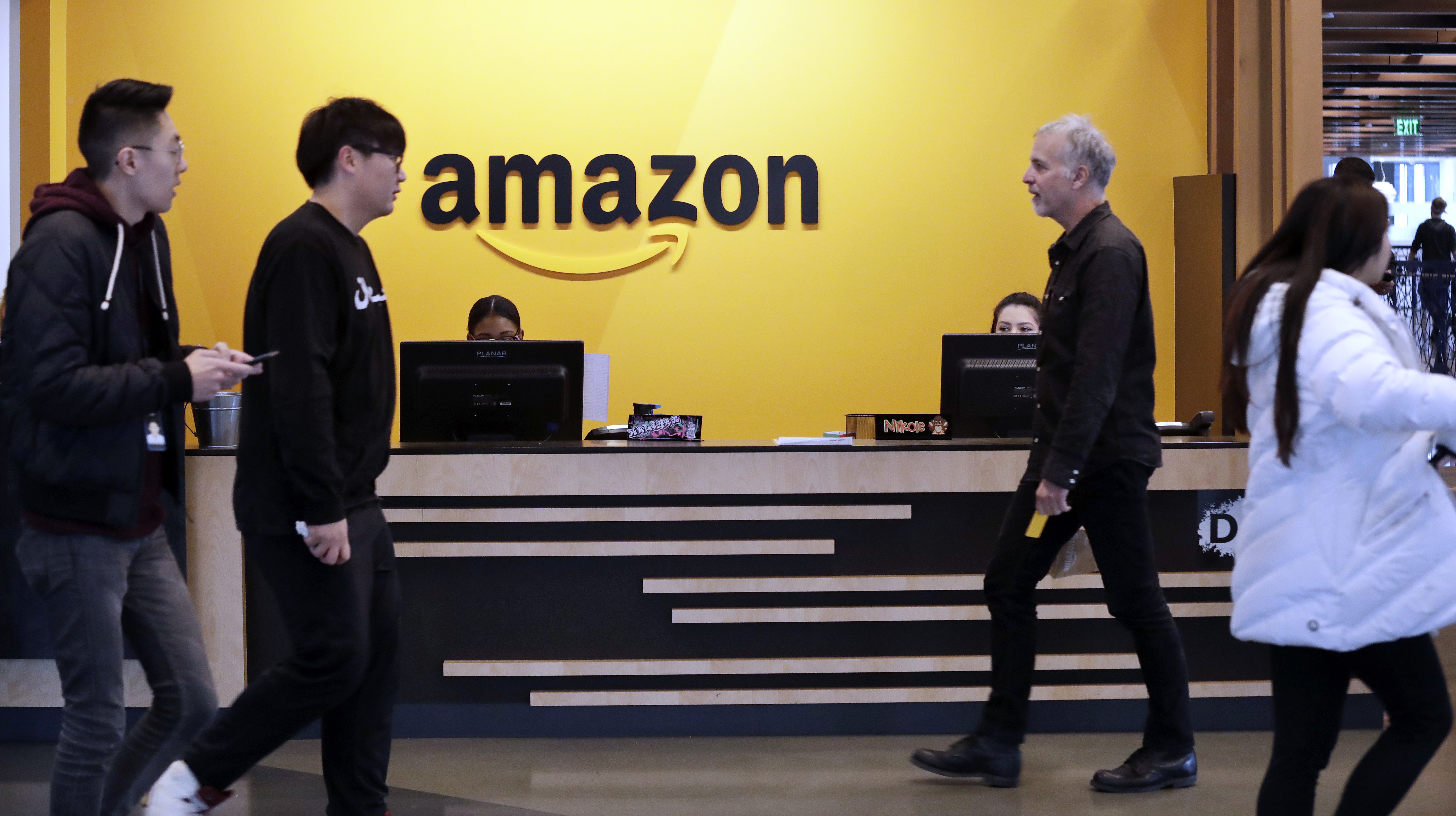 FILE - In this Nov. 13, 2018 file photo, employees walk through a lobby at Amazon's headquarters in Seattle. On Friday, May 3, 2019, shares in Amazon are moving higher after billionaire investor Warren Buffett said his firm has been buying the online retailer. (AP Photo/Elaine Thompson)