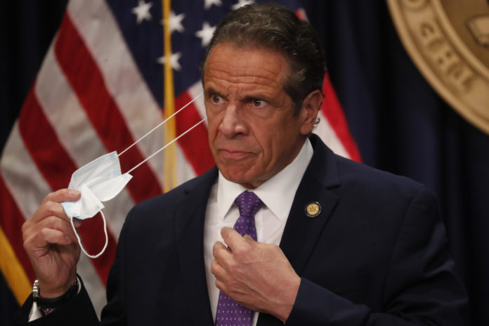 Gov. Andrew Cuomo takes off his face mask before a news conference in New York on Monday, April 19, 2021. Cuomo is allowing more people to go inside museums, movie theaters and indoor big sports arenas as the latest data suggests the state's massive vaccination campaign is curbing COVID-19 infection levels. (Shannon Stapleton/Pool via AP)