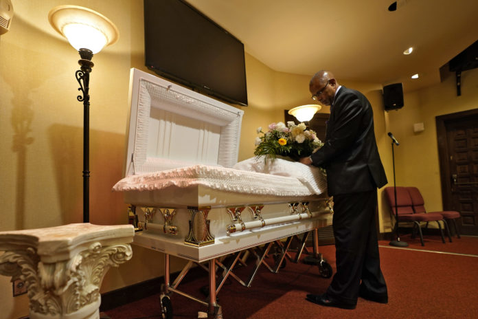 Wayne Bright, funeral director at Wilson Funeral Home, arranges flowers on a casket before a service Thursday, Sept. 2, 2021, in Tampa, Fla. Bright has seen grief piled upon grief during the latest COVID-19 surge as Florida is in the grip of its deadliest wave since the pandemic began, a disaster driven by the highly contagious delta variant. (AP Photo/Chris O'Meara)