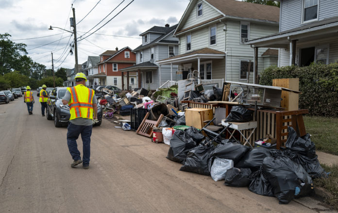 Utility workers walk along a street piled with debris from flood damage caused by the remnants of Hurricane Ida in Manville, N.J., Sunday, Sept. 5, 2021. Flood-stricken families and business owners across the Northeast are hauling waterlogged belongings to the curb and scraping away noxious mud as cleanup from Ida moves into high gear. (AP Photo/Craig Ruttle)