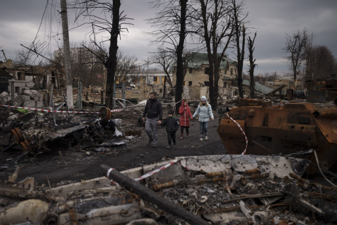 A family walks amid destroyed Russian tanks in Bucha, on the outskirts of Kyiv, Ukraine, Wednesday, April 6, 2022. (AP Photo/Felipe Dana)