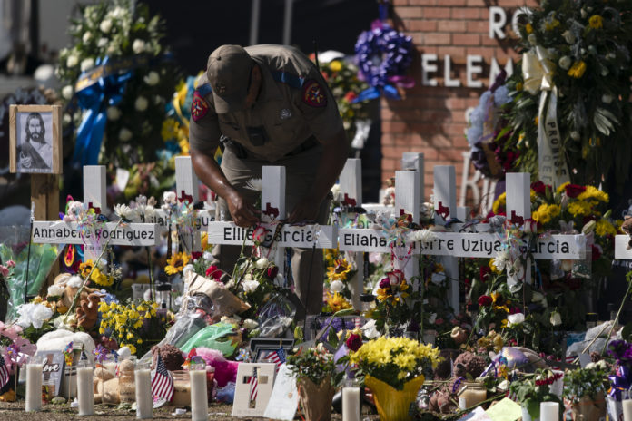 A state trooper places a tiara on a cross honoring Ellie Garcia, one of the victims killed in this week's elementary school shooting in Uvalde, Texas Saturday, May 28, 2022. (AP Photo/Jae C. Hong)