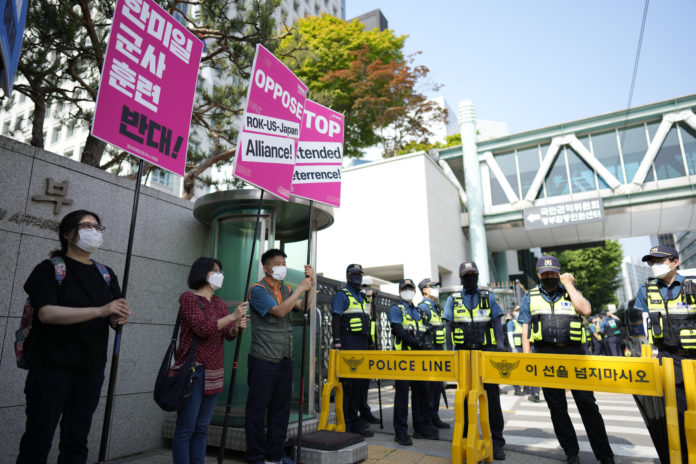 Protesters hold signs as police officers stand guard during a rally outside of Foreign Ministry where a trilateral meeting among the United States, South Korea and Japan, is held in Seoul, South Korea, Friday, June 3, 2022. (AP Photo/Lee Jin-man)